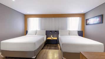 A hotel room with two single beds, a small bedside table, a nightstand, and a large window with curtains.