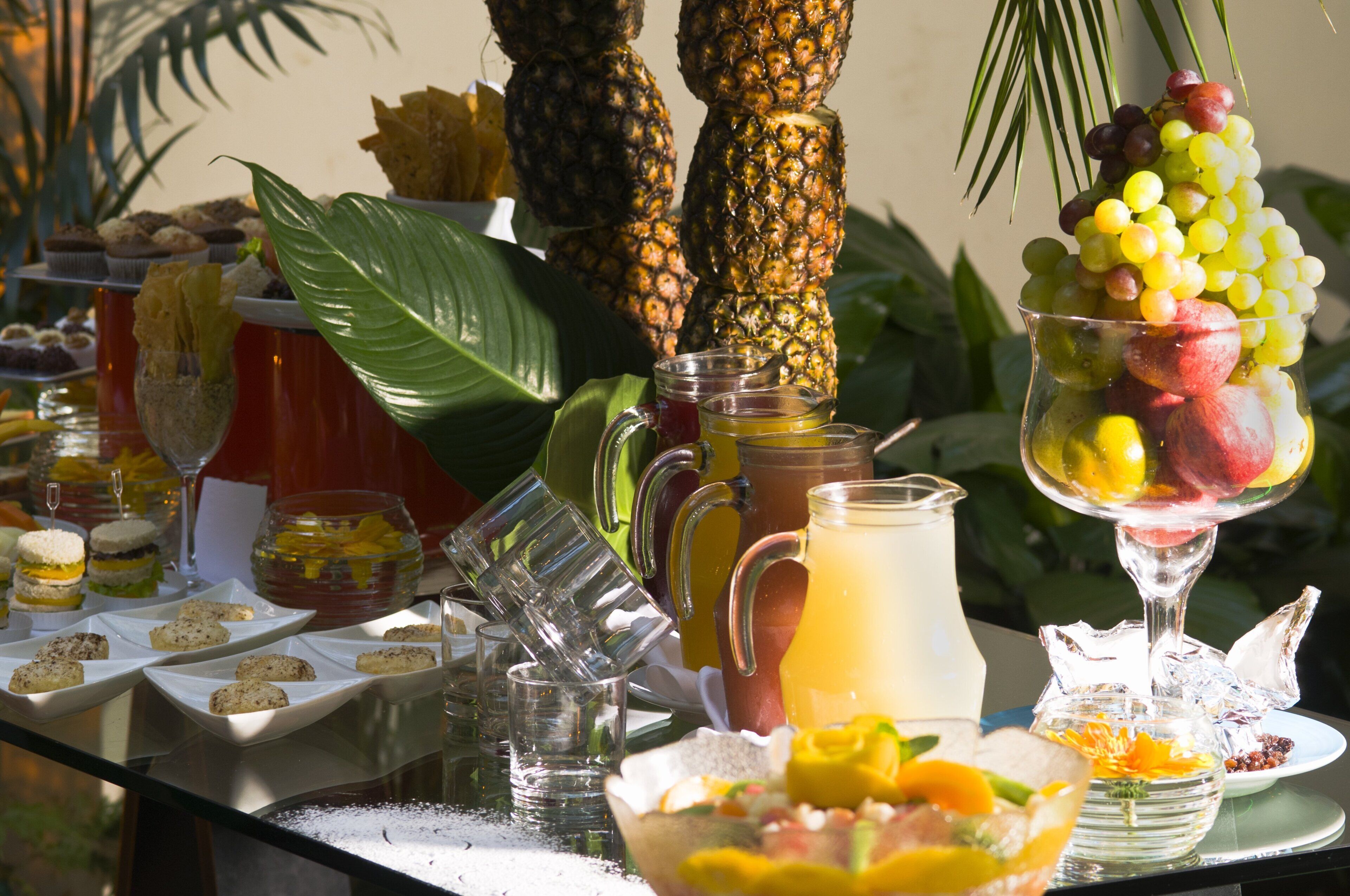 Mesa de buffet con diversos alimentos, bebidas y un fondo tropical.