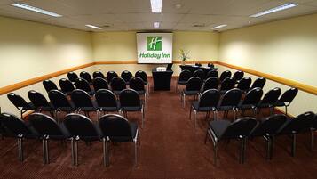 A conference room with rows of black chairs, a podium, and a screen displaying the Holiday Inn logo.