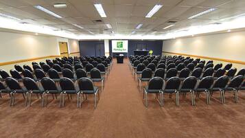 A conference room with rows of chairs facing a podium, a carpeted floor, and a Holiday Inn sign on the wall.
