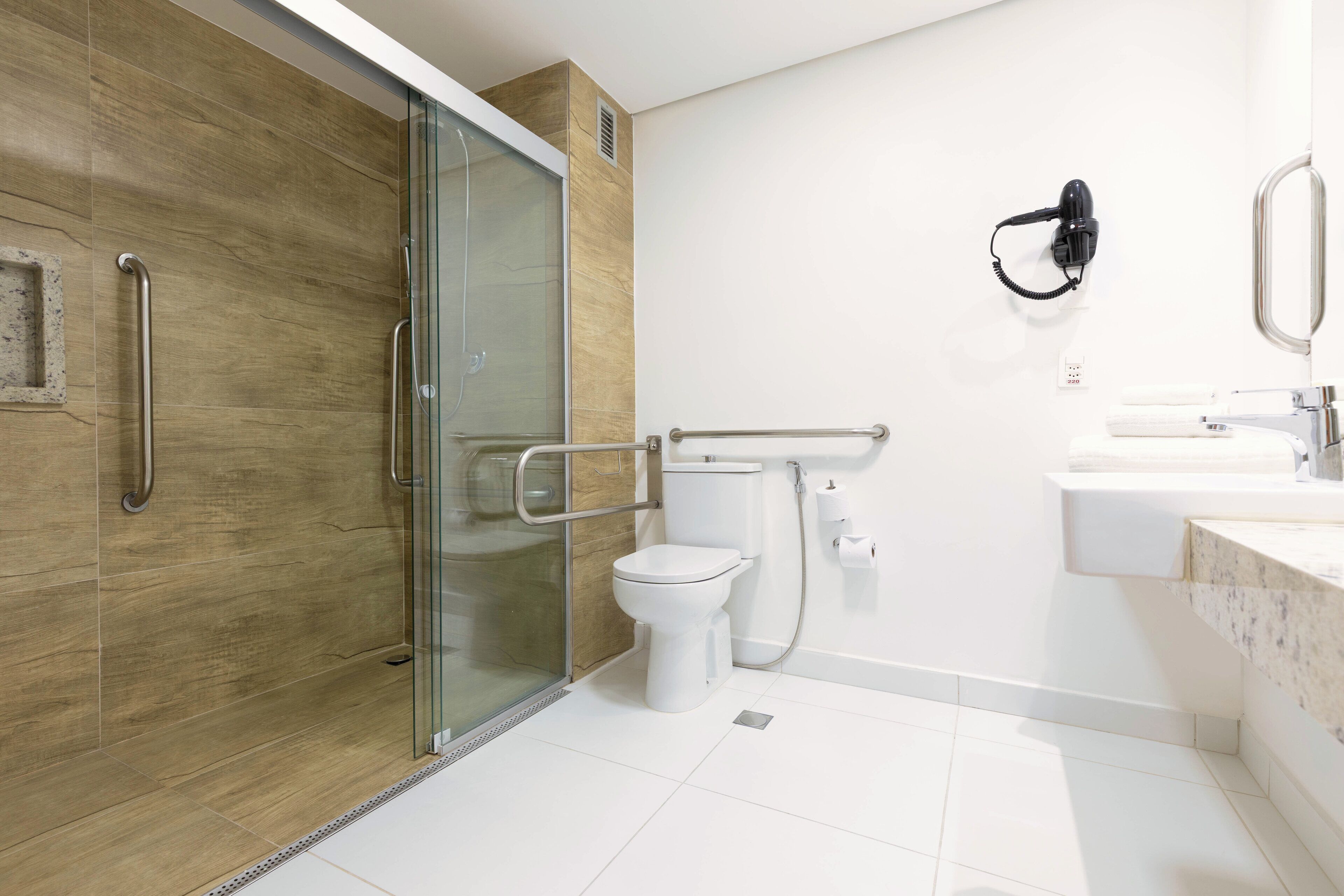 A modern bathroom with a glass shower enclosure, a white toilet, and a sink with a towel rack.