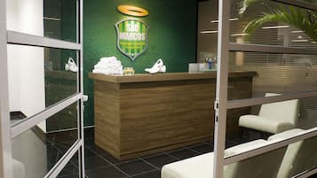 Een receptiezone met een houten balie, een groene wand met een logo en een zithoek met stoelen.