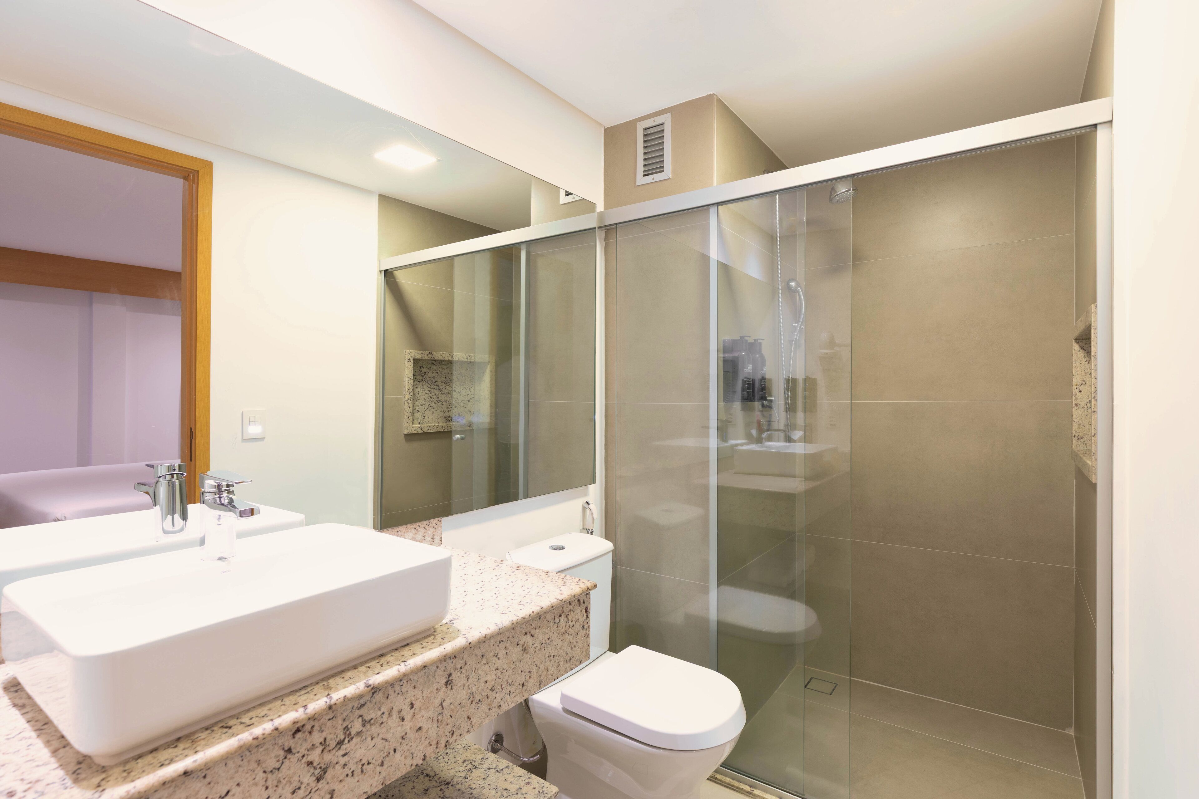 Un baño moderno con un lavamanos grande de color blanco, un inodoro y una ducha con mampara de vidrio.