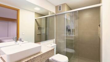 Un baño moderno con un lavamanos grande de color blanco, un inodoro y una ducha con mampara de vidrio.