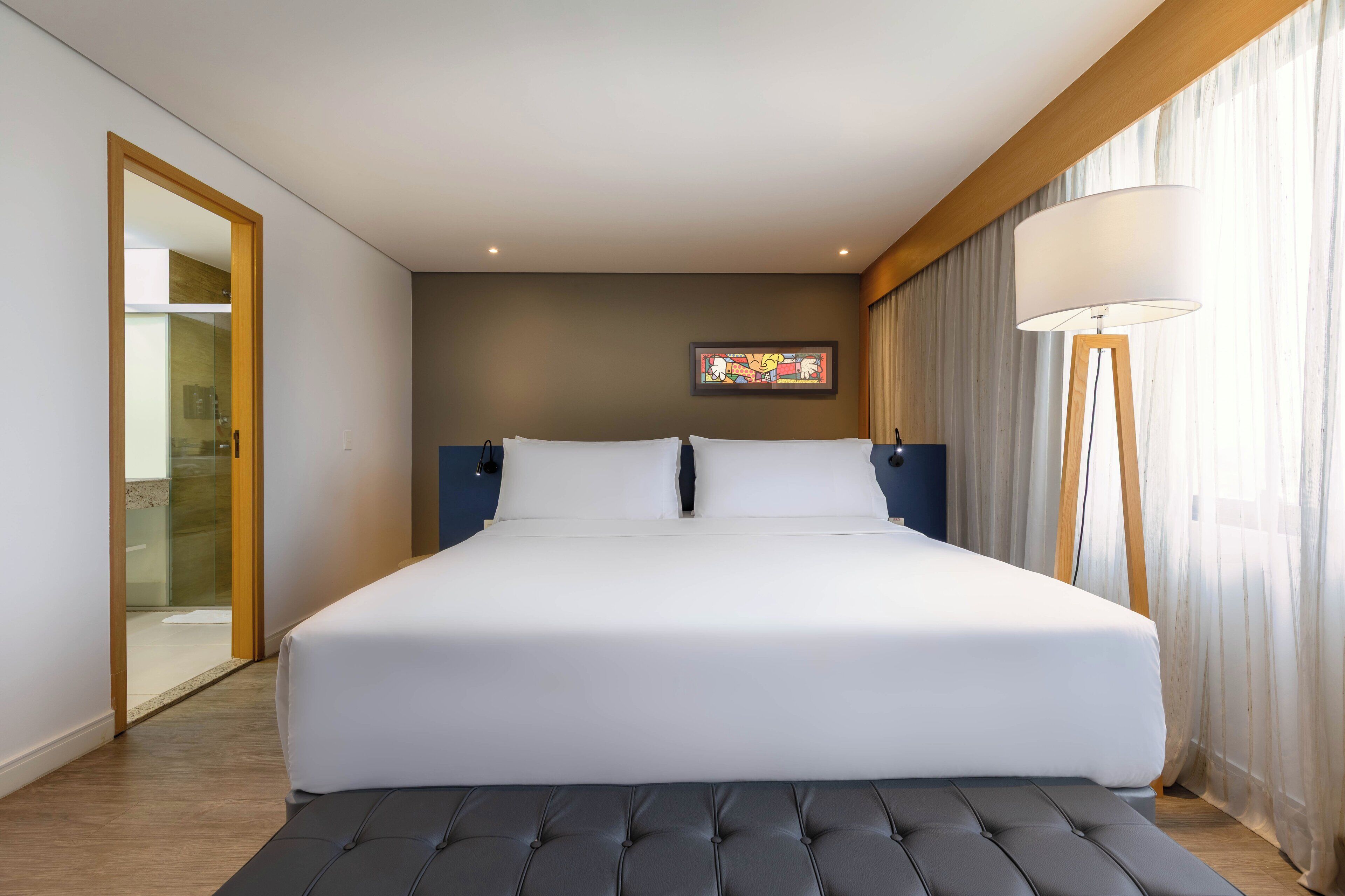 Una habitación de hotel moderna con una cama grande, una mesita de noche, una lámpara de pie y un cuadro en la pared.