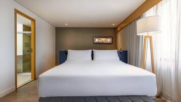 Una habitación de hotel moderna con una cama grande, una mesita de noche, una lámpara de pie y un cuadro en la pared.