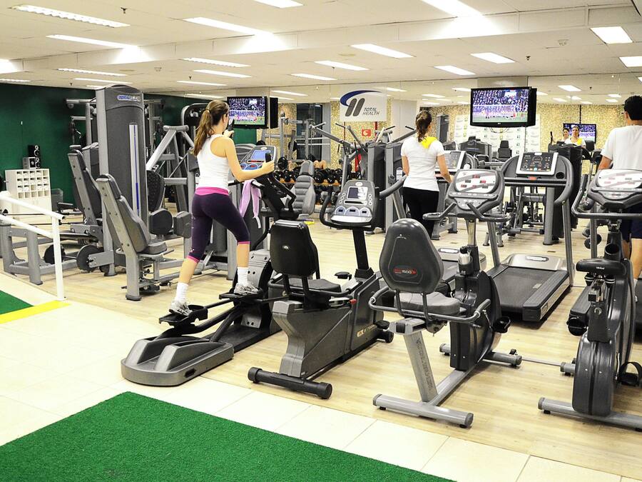 A gym with various exercise equipment, including treadmills and weight machines, and multiple television screens displaying sports events.