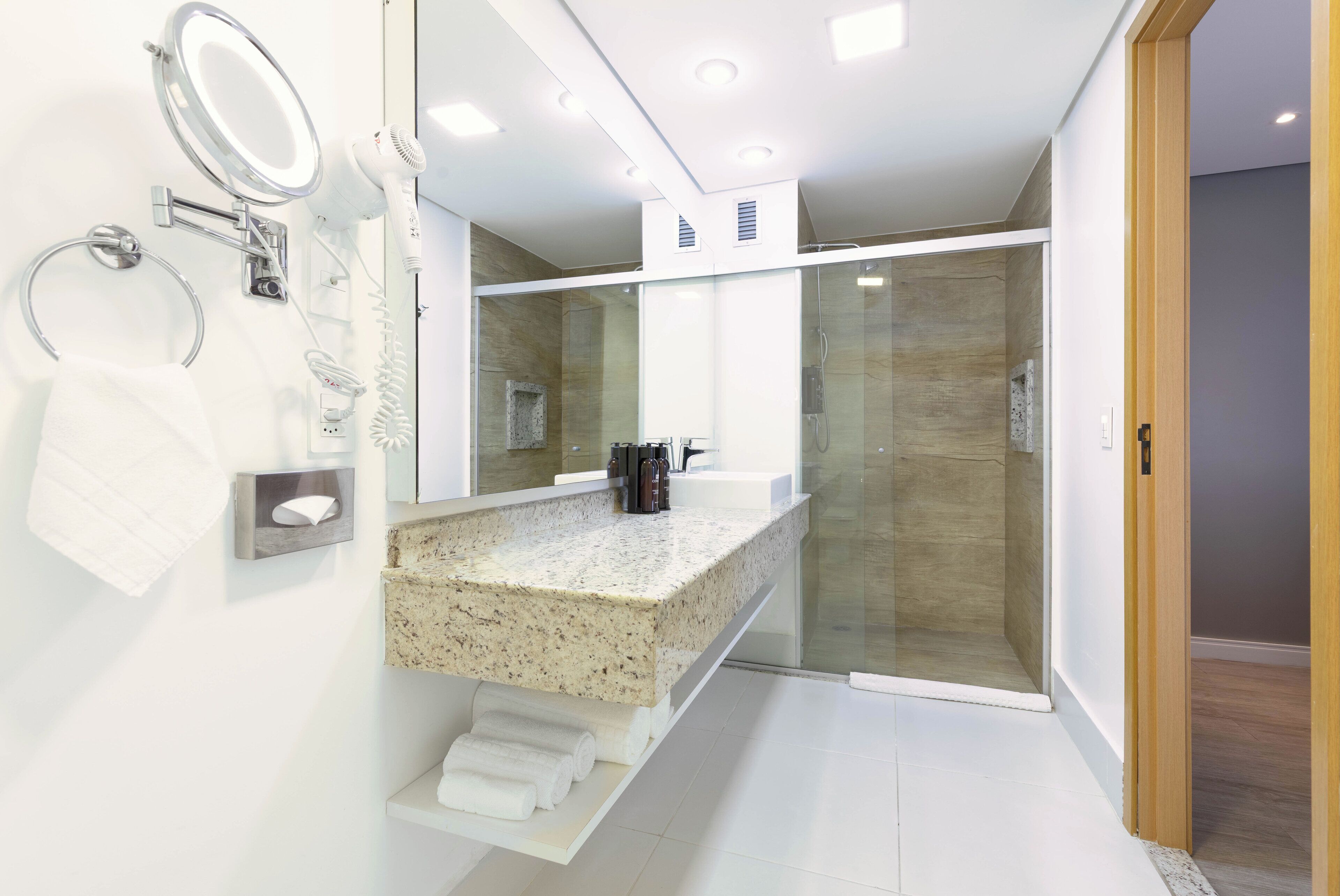 A modern bathroom with a granite countertop, a glass shower enclosure, and a built-in mirror.