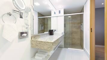A modern bathroom with a granite countertop, a glass shower enclosure, and a built-in mirror.