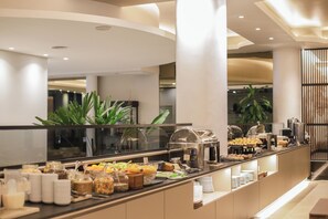A buffet area with various food items and containers, including fruits, pastries, and condiments. - Plaza Real Suites Hotel (Rosario)