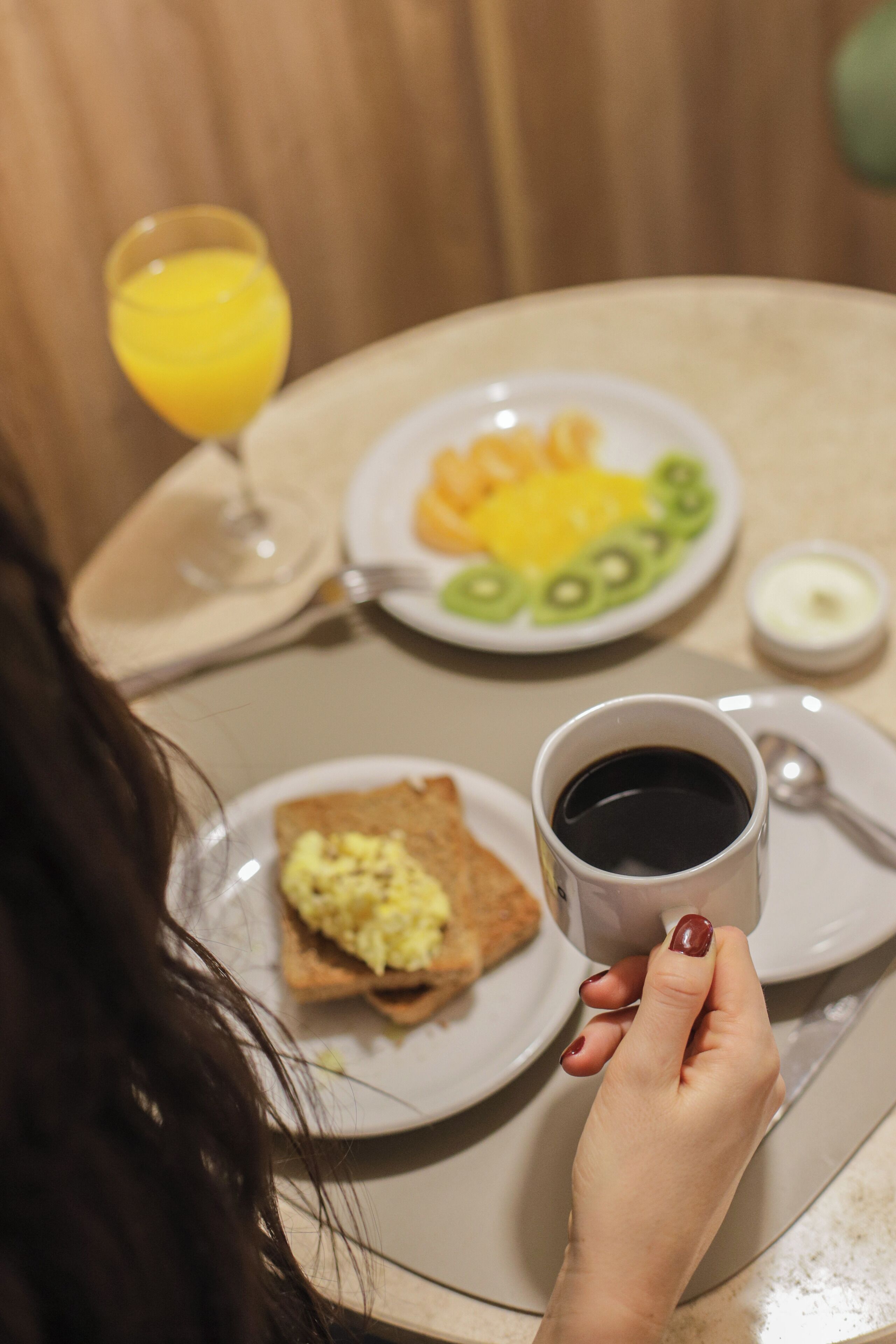 Une table mise pour le petit-déjeuner avec une assiette d’œufs brouillés, des toasts et un verre de jus d’orange.