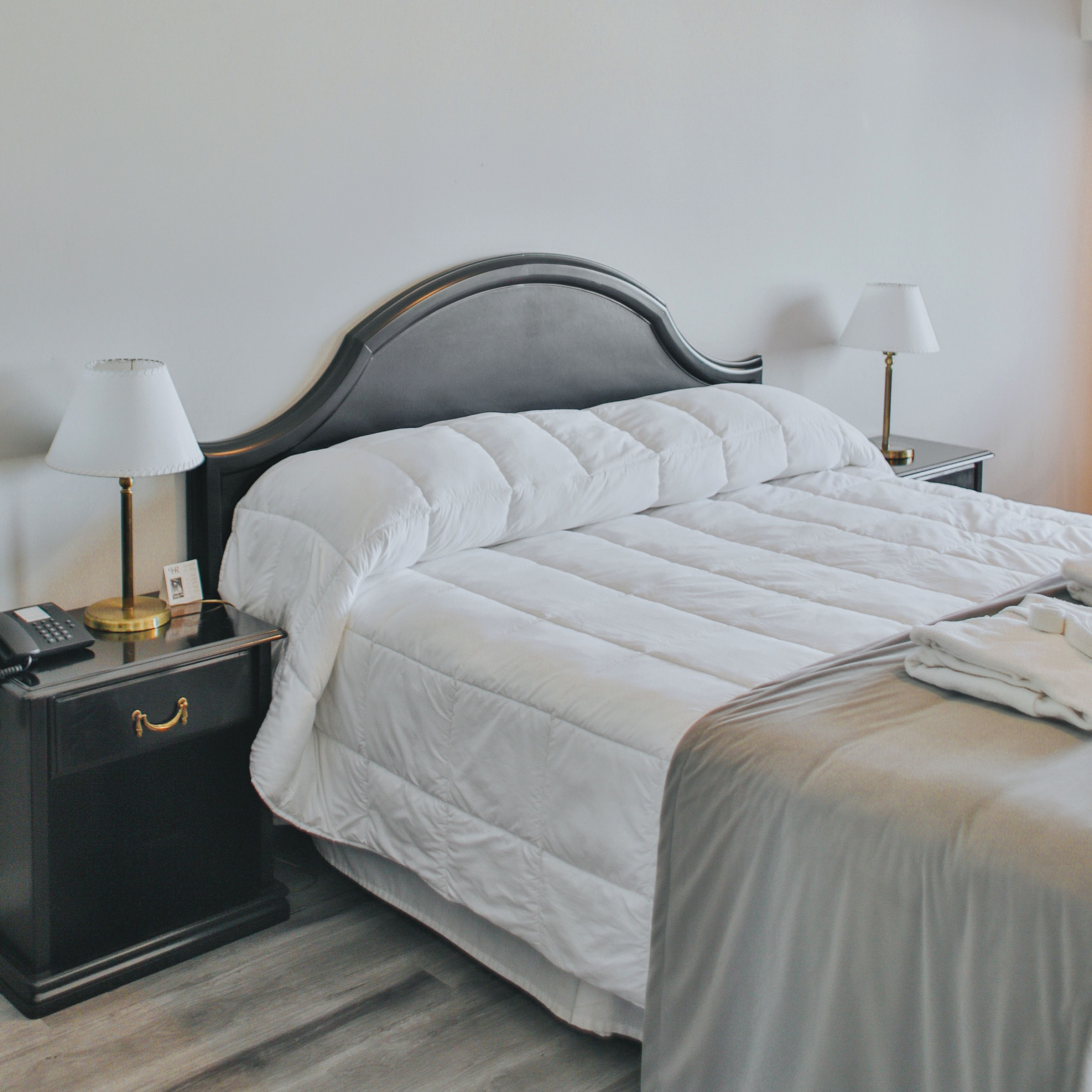 A neatly made bed with a dark headboard, two bedside tables with lamps, and a small drawer with a telephone.