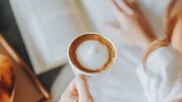 Une personne tenant une tasse de café, avec un livre et une assiette de pâtisseries en arrière-plan.