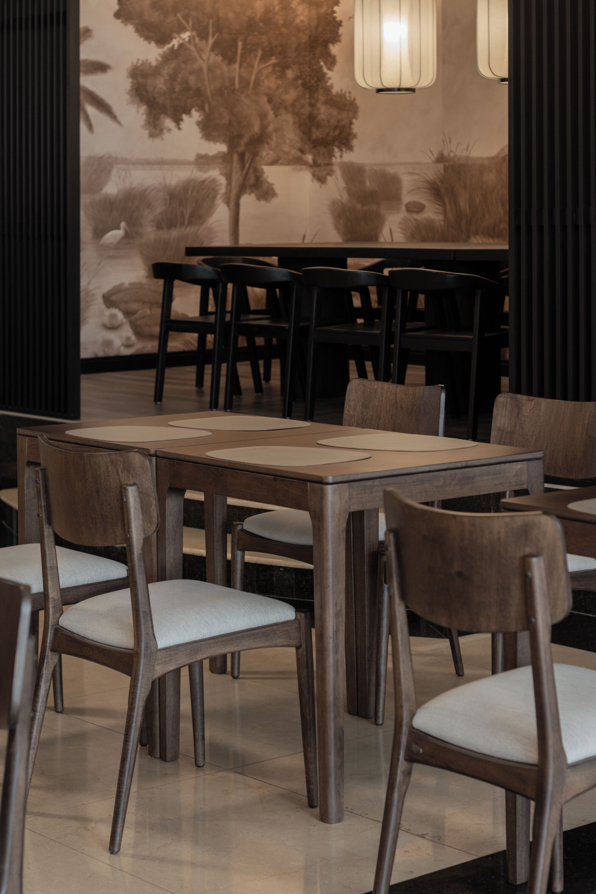 L’intérieur d’un restaurant avec des tables et des chaises en bois, une fresque murale et des luminaires suspendus.