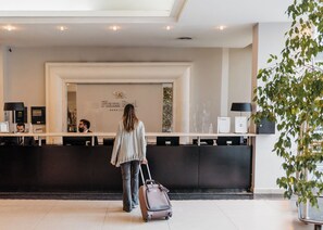 A reception desk with a sign reading "Plaza Real" and a woman with luggage approaching. - Plaza Real Suites Hotel (Rosario)