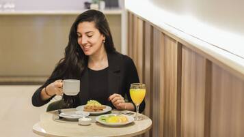 Una persona sentada a una mesa redonda con una taza y un vaso de jugo de naranja. La mesa está servida con platos de comida.