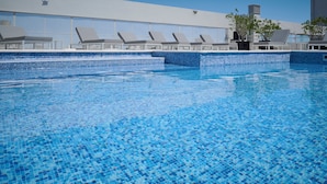 Ein Swimmingpool mit klarem, blauem Wasser, umgeben von Liegestühlen und einem modernen Gebäude im Hintergrund.