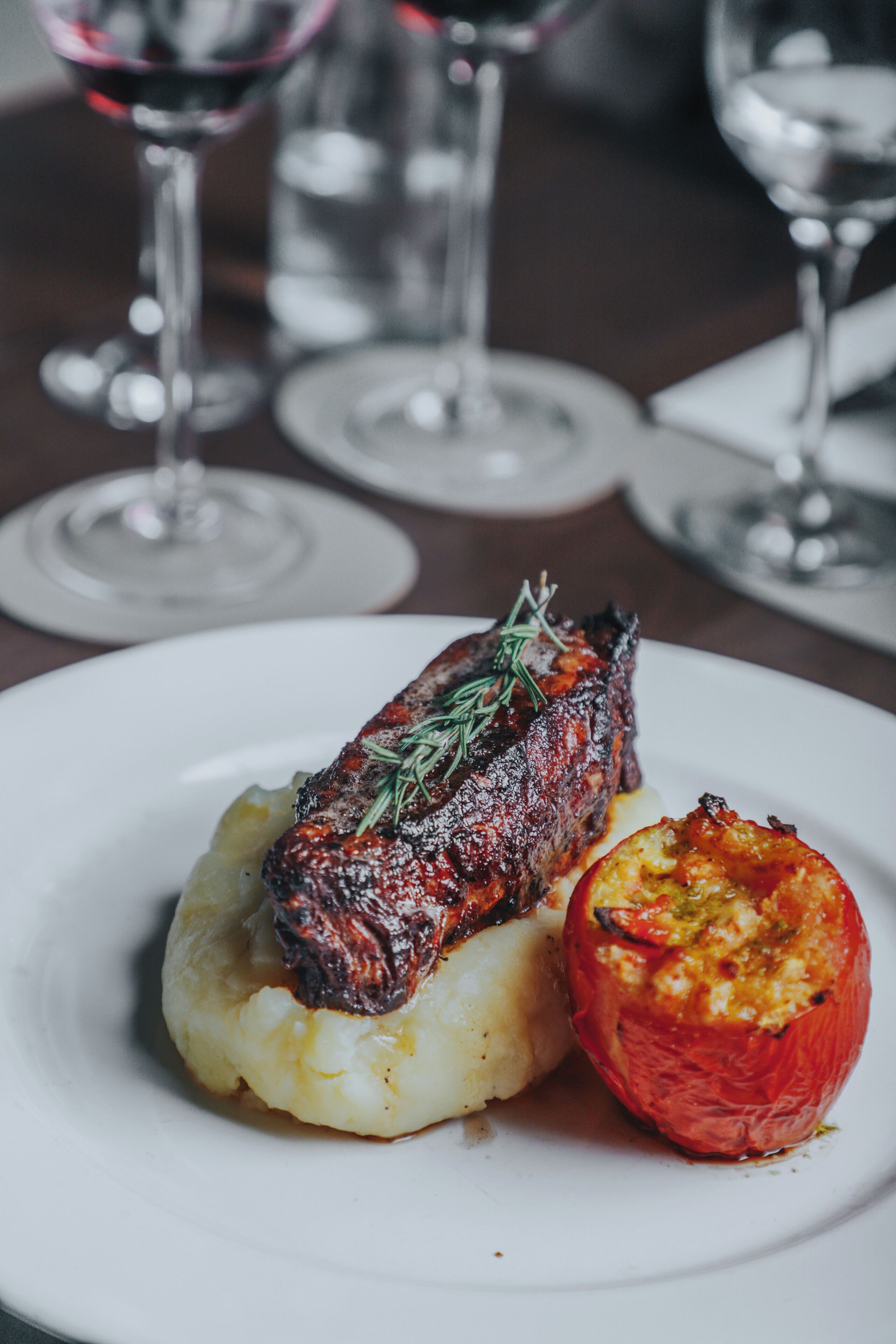 A plate with a roasted meat, mashed potatoes, and a roasted tomato.