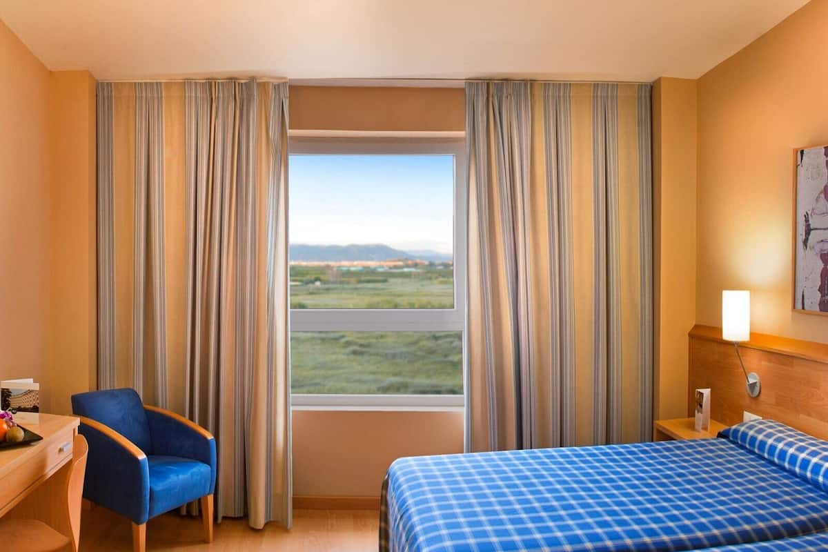 Habitación de hotel con cama, escritorio, silla y vistas a un paisaje por la ventana.