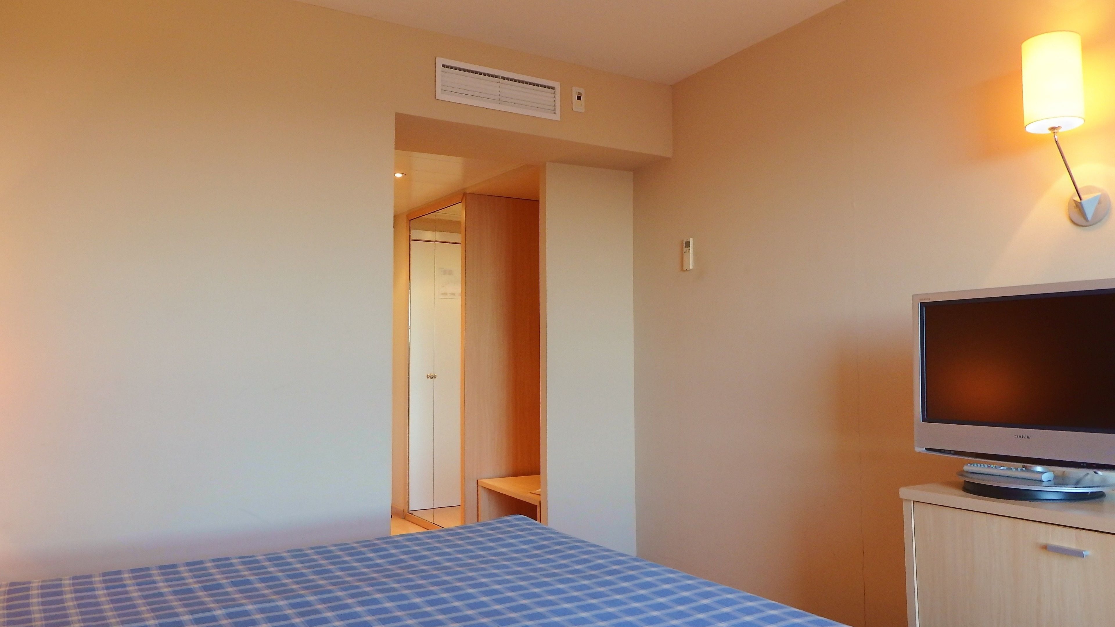 A hotel room with a bed, a television on a stand, and a door leading to another room.