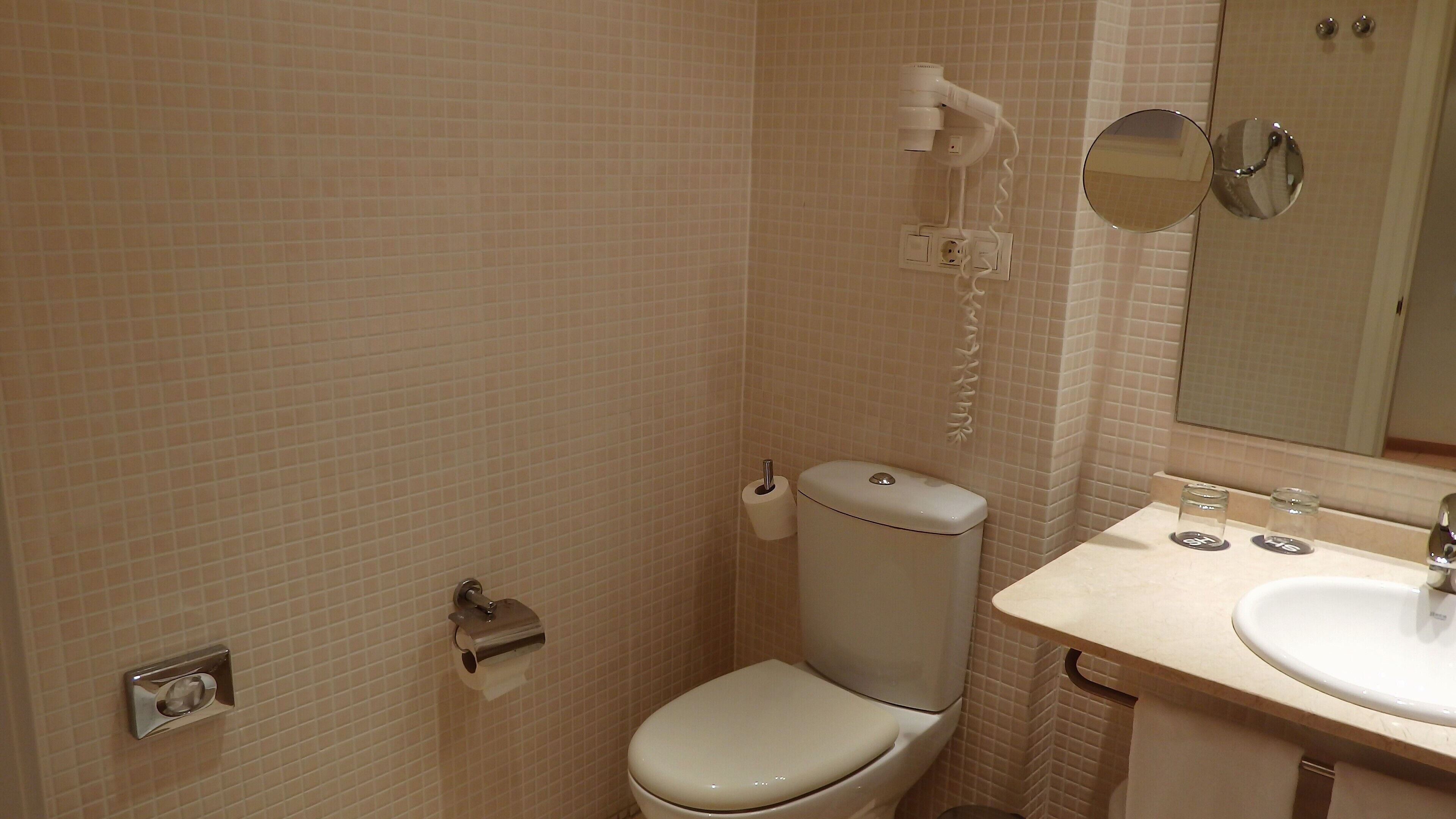 Un baño con inodoro, lavabo, espejo y secador de pelo en la pared.