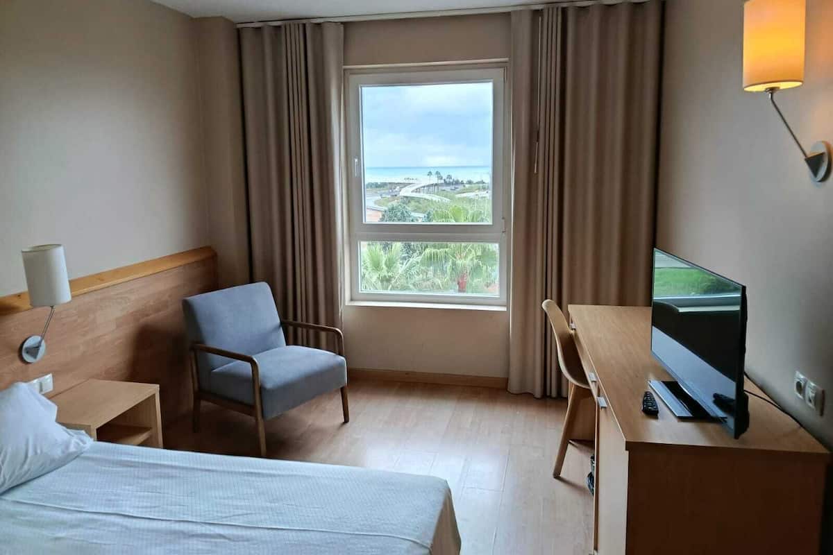 Habitación de hotel con cama, escritorio con televisor, una silla y vista a un puente y follaje.