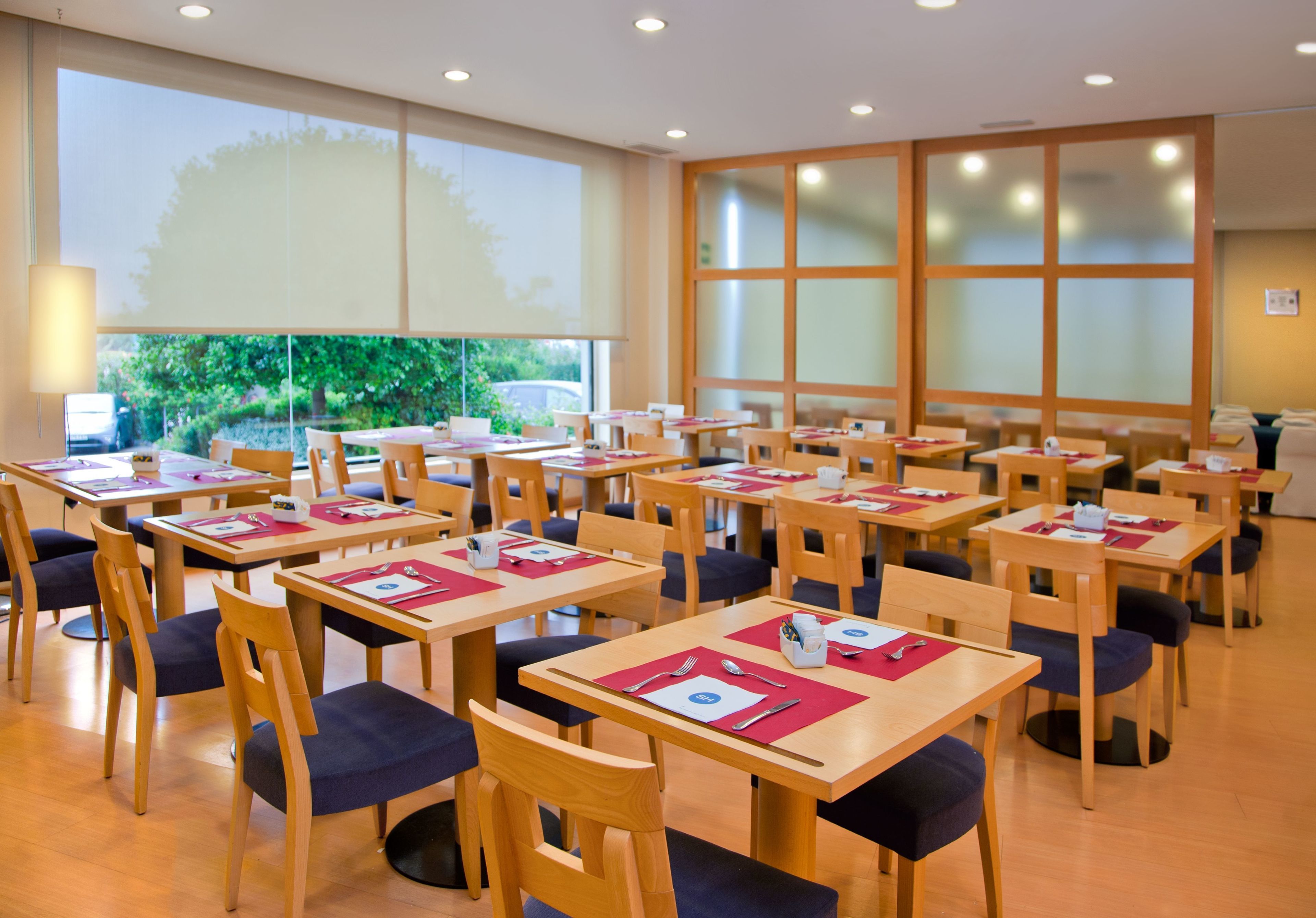 Comedor con mesas y sillas, ventanas amplias y vista a zonas verdes.