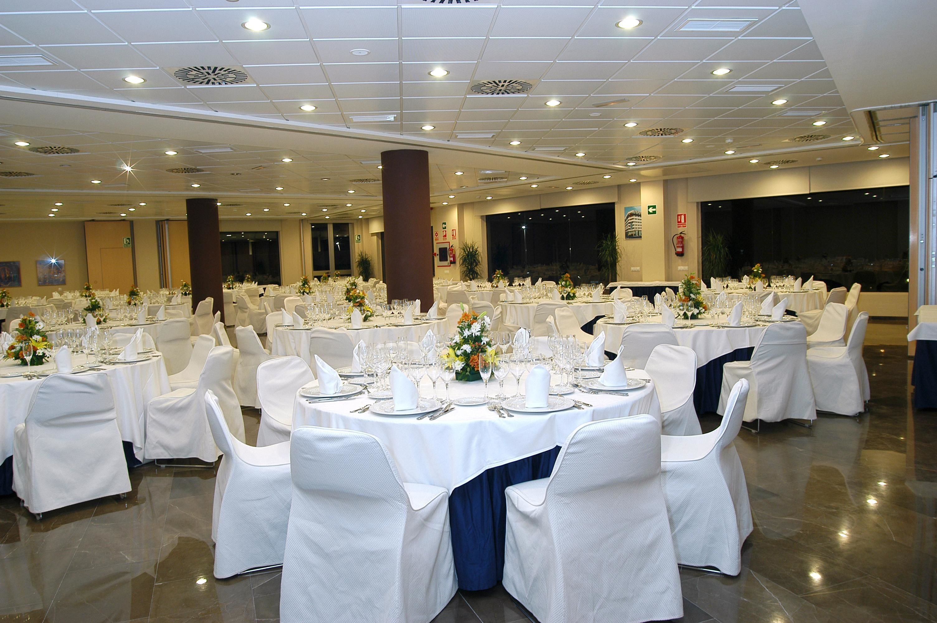 A banquet hall with round tables set for a formal event, featuring white tablecloths, chairs, and floral centerpieces.