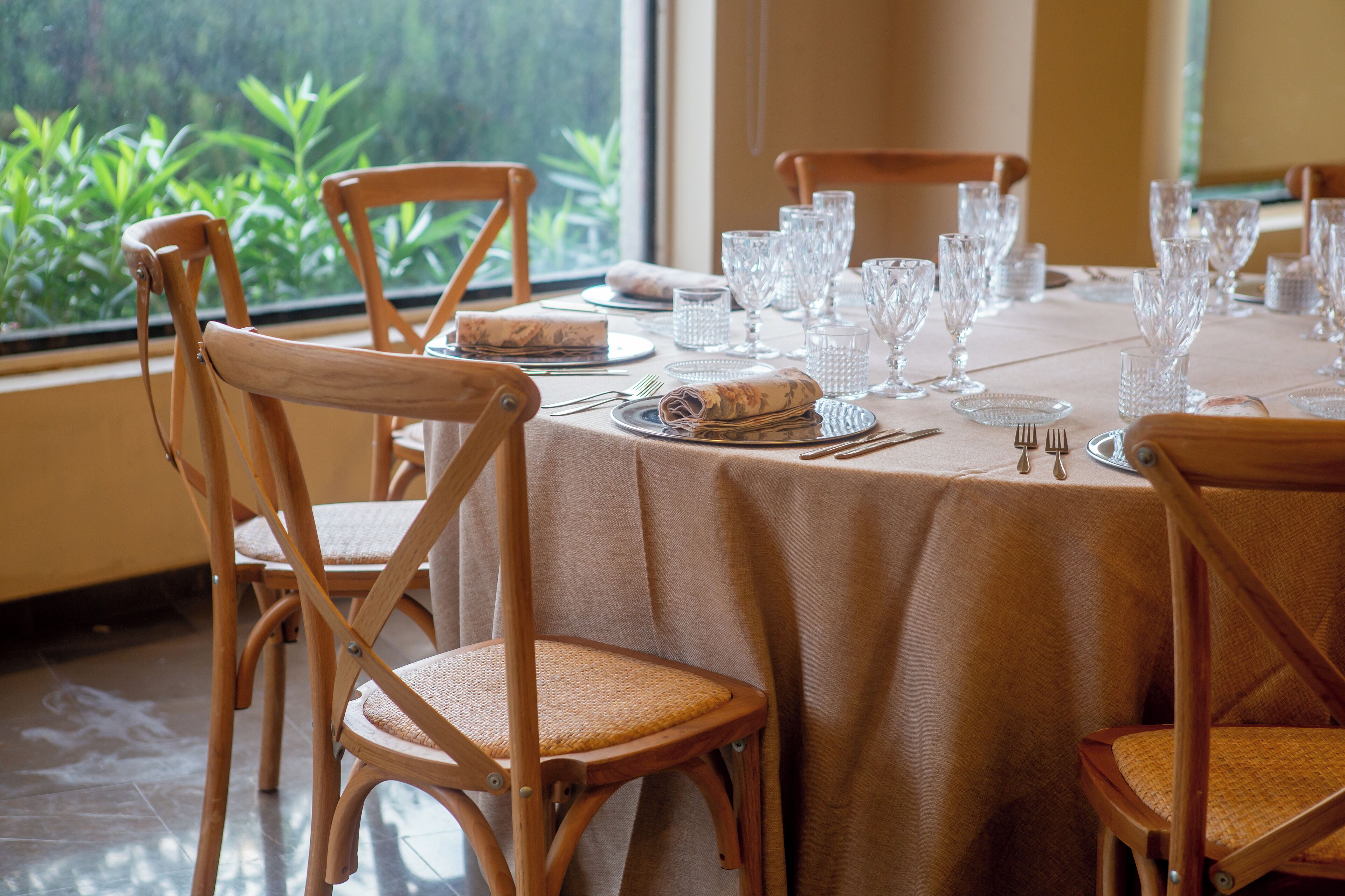 A dining table set with glassware, plates, and cutlery, surrounded by wooden chairs with woven seats.