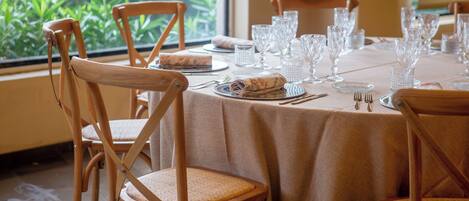 Mesa de comedor dispuesta con cristalería, platos y cubiertos, rodeada de sillas de madera con asientos de mimbre.