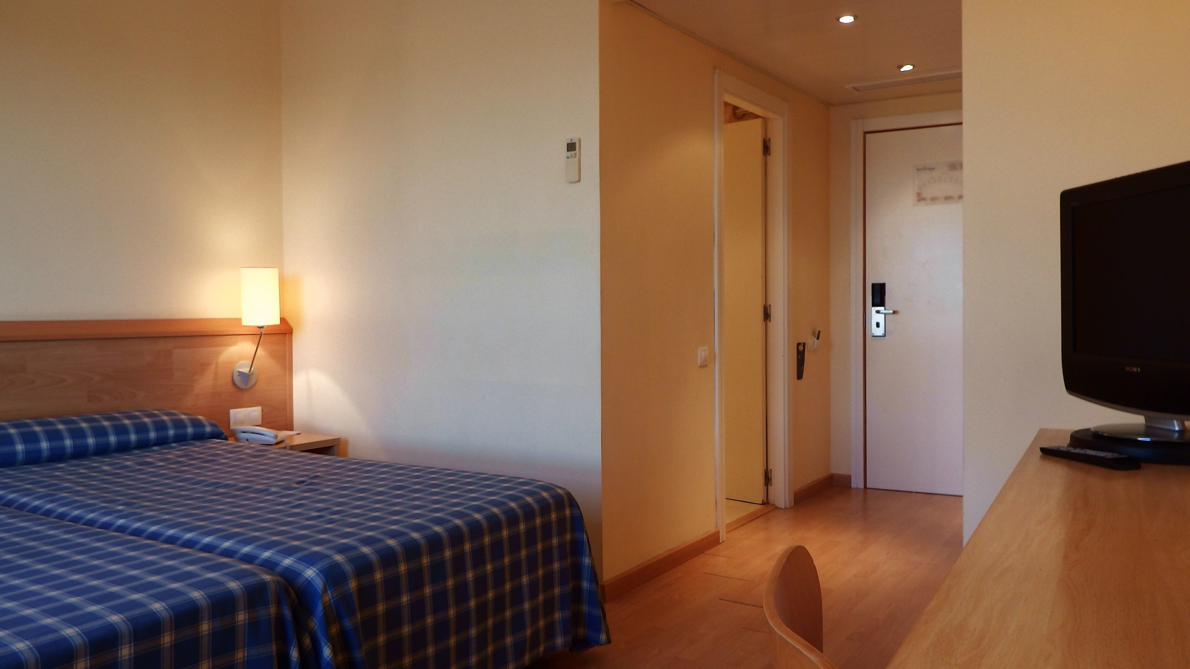 A hotel room with a bed, a TV, a bedside table, and a door.