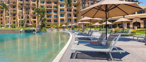 A resort pool area with lounge chairs and umbrellas, surrounded by a multi-story hotel building.