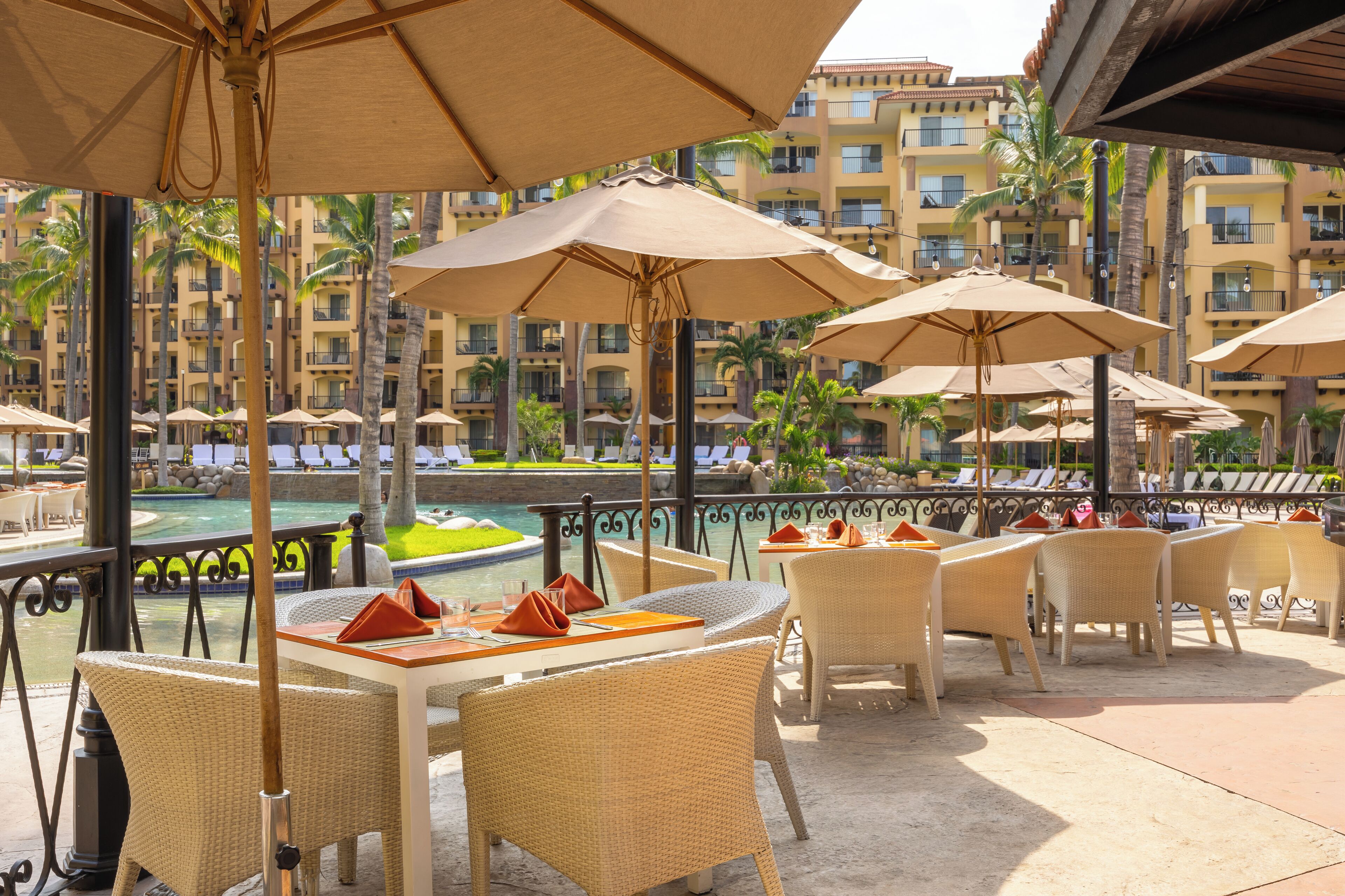 A poolside area with wicker furniture, umbrellas, and a view of a pool and buildings.