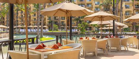 A poolside area with wicker furniture, umbrellas, and a view of a pool and buildings.