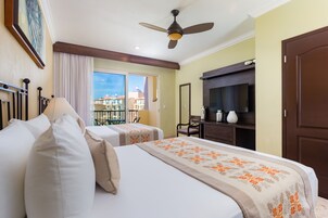 Habitación de hotel con dos camas, ventilador de techo, televisión y balcón con vista a edificios.
