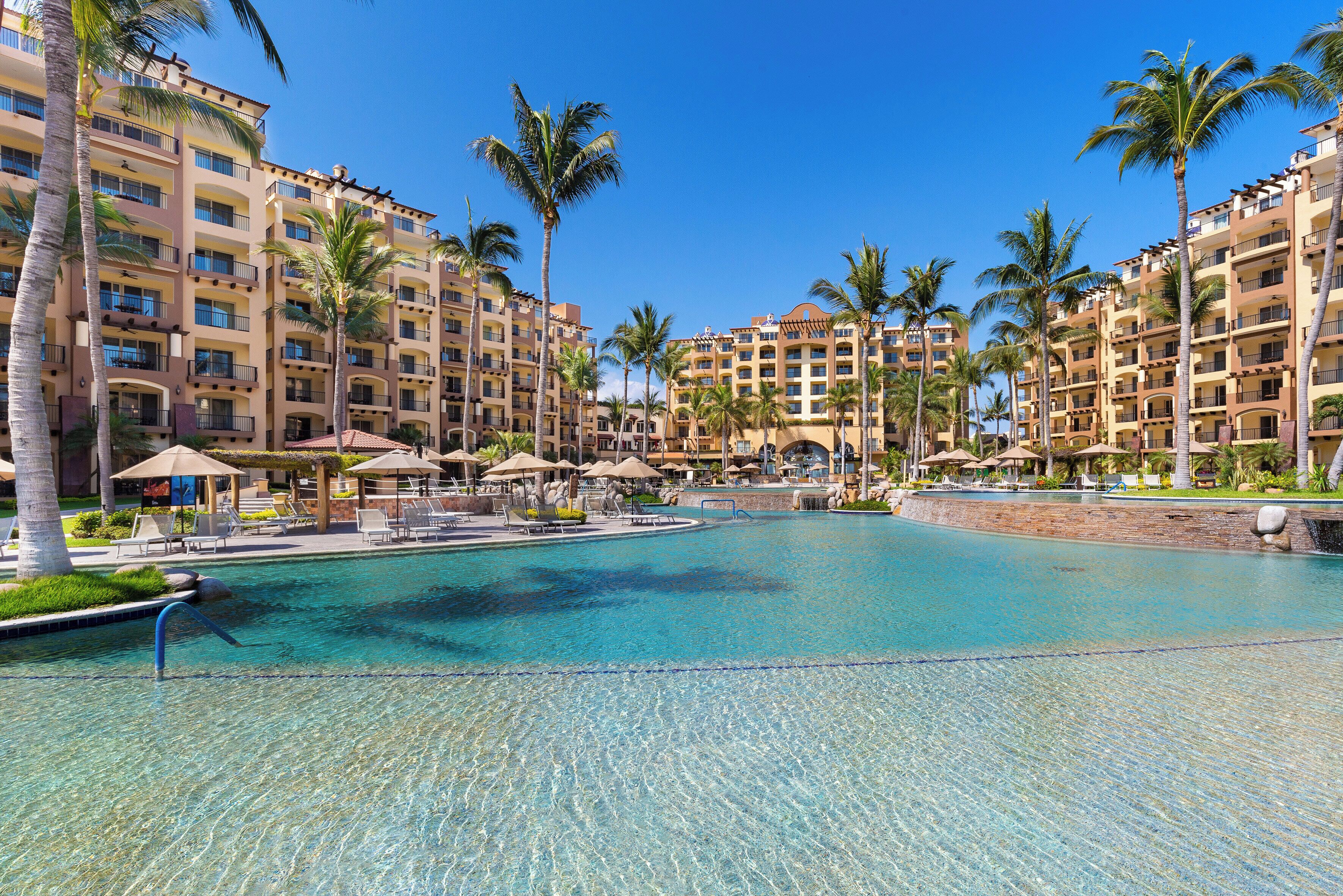 A resort with a large pool, palm trees, and multiple-story buildings.