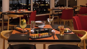 A restaurant with a view of palm trees and a beach, sushi dishes, and a martini glass on the table. - Villa Del Palmar Flamingos Beach Resort and Spa (Nuevo Nayarit)
