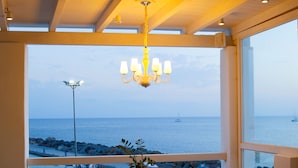 A dining area with a table and chairs, a chandelier, and a view of the sea through large windows. - Notos Therme And Spa by Mr and Mrs White (Santorini)
