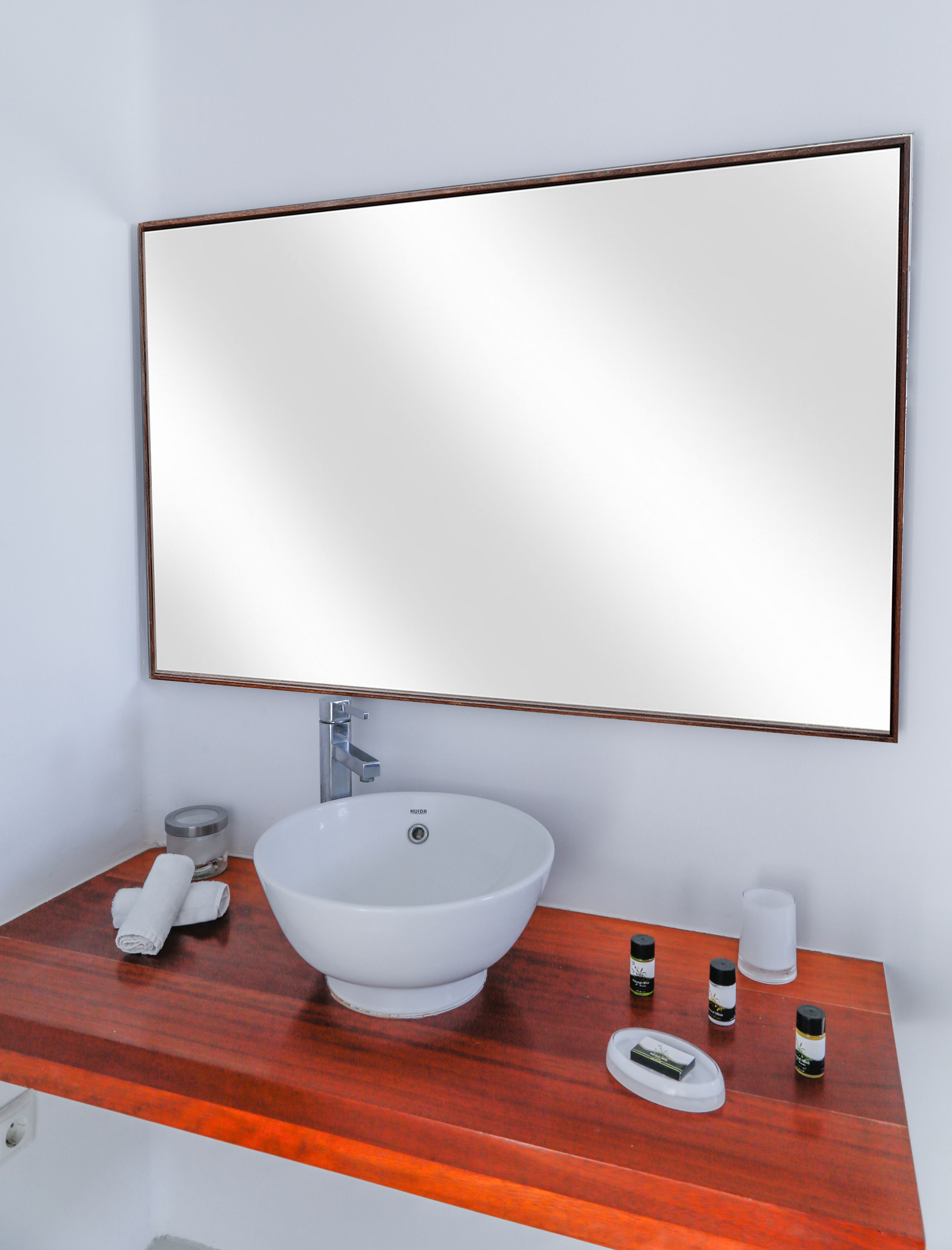 Un baño con un lavamanos blanco, un mueble de tocador de madera, un espejo grande y artículos de aseo en la encimera.