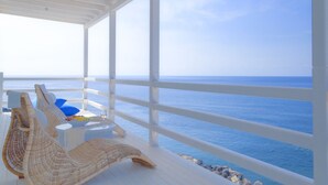 A covered outdoor area with wicker furniture and a table, overlooking a body of water. - Notos Therme And Spa by Mr and Mrs White (Santorini)