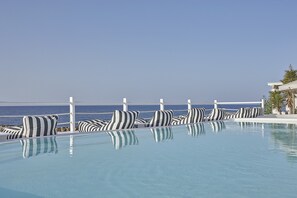 A pool with striped cushions and a view of the ocean. - Notos Therme And Spa by Mr and Mrs White (Santorini)