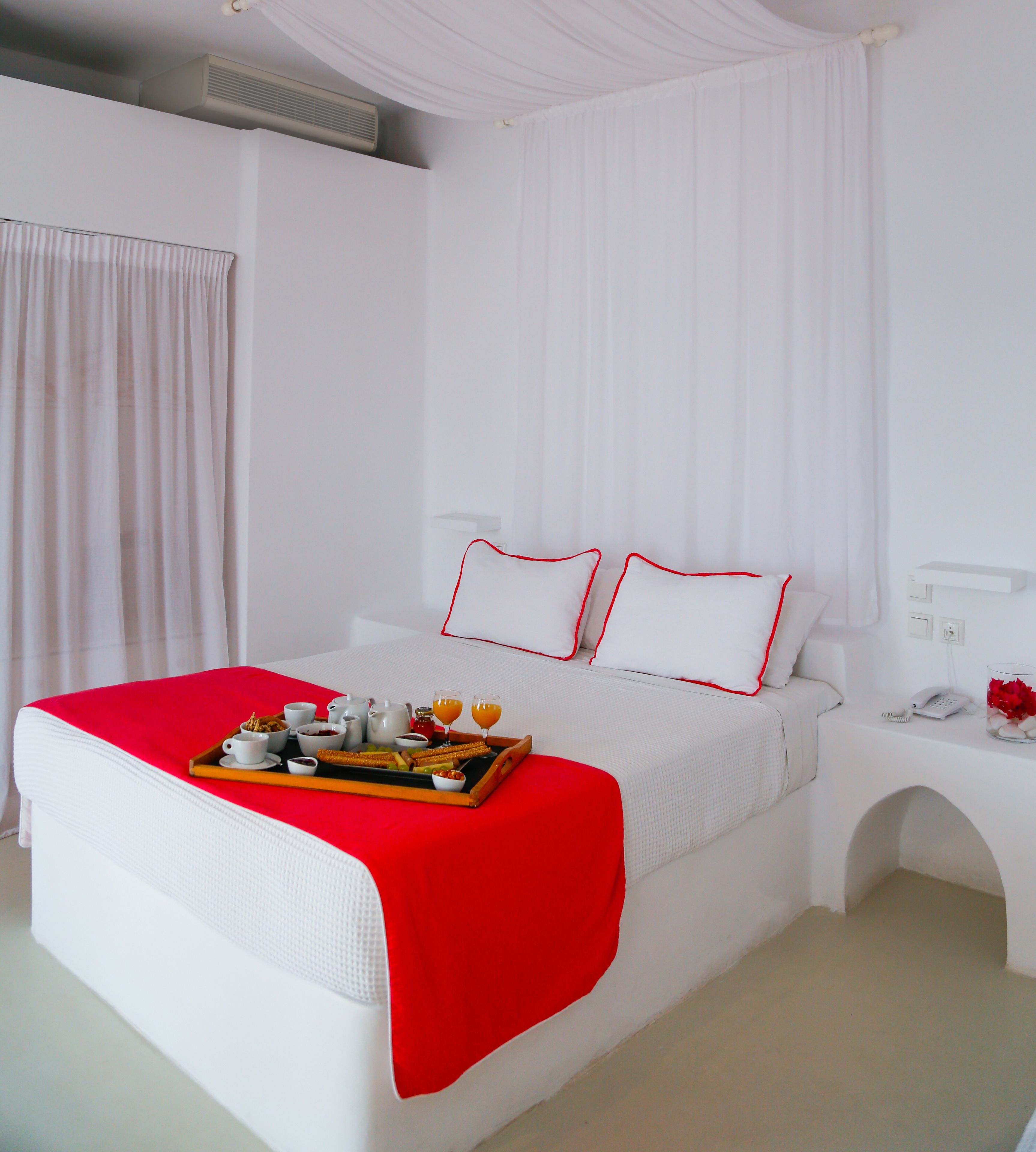Ein Hotelzimmer mit einem großen Bett, weißer Bettwäsche, einer roten Decke und einem Tablett mit Frühstücksartikeln.