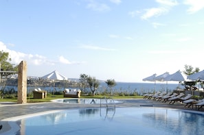 Relax by the serene pool overlooking the sea and distant mountains, surrounded by lounge chairs and umbrellas.