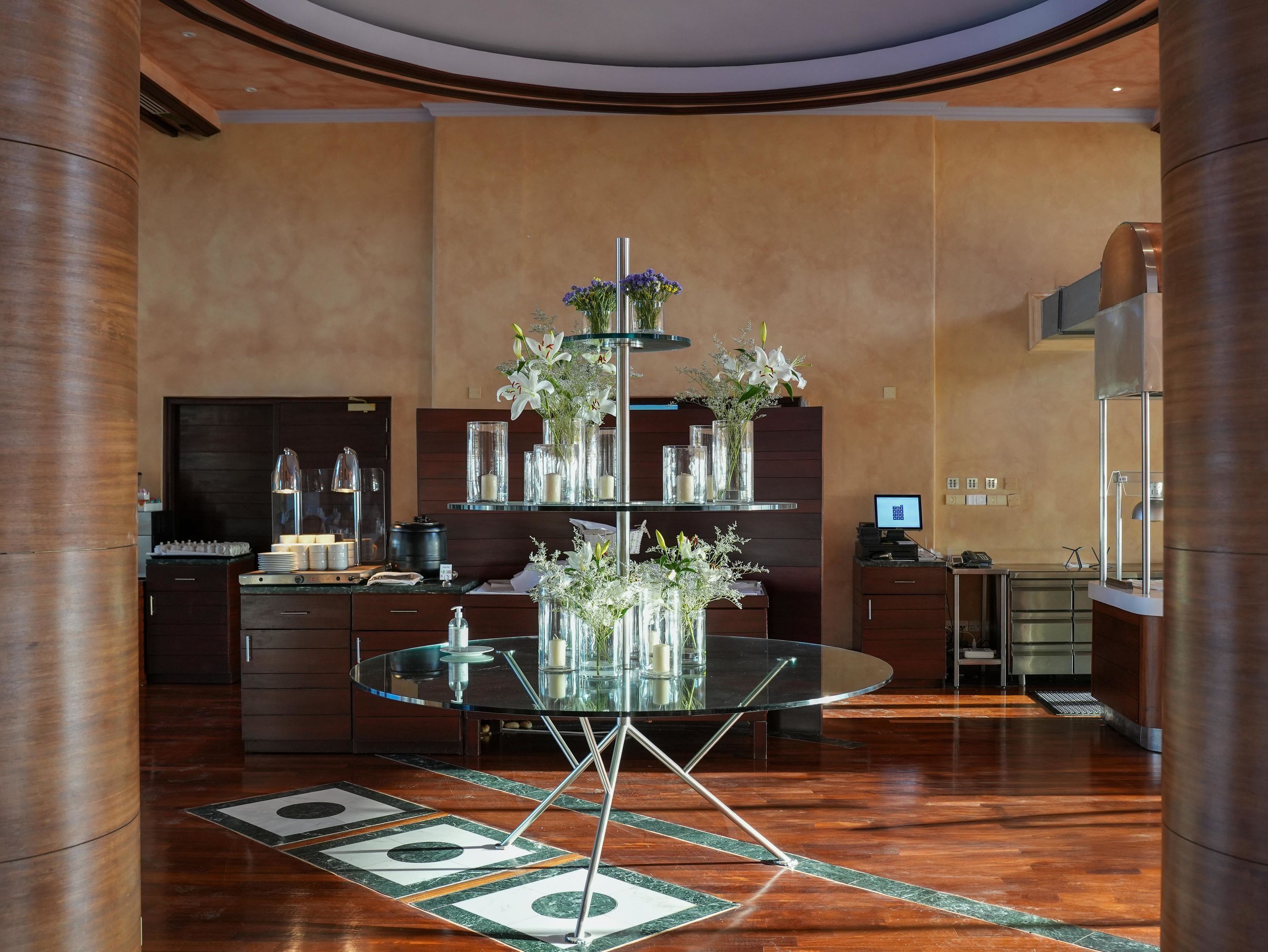 A modern hotel lobby with a glass table, wooden flooring, and a reception desk with a computer.