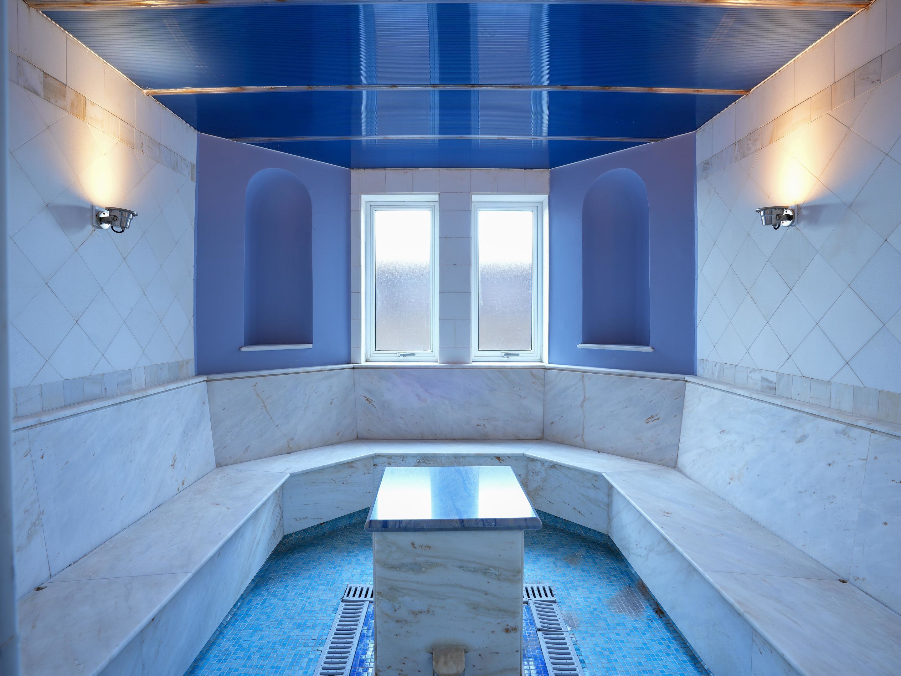 A spa room with a marble floor, a central pool, and two windows with frosted glass.