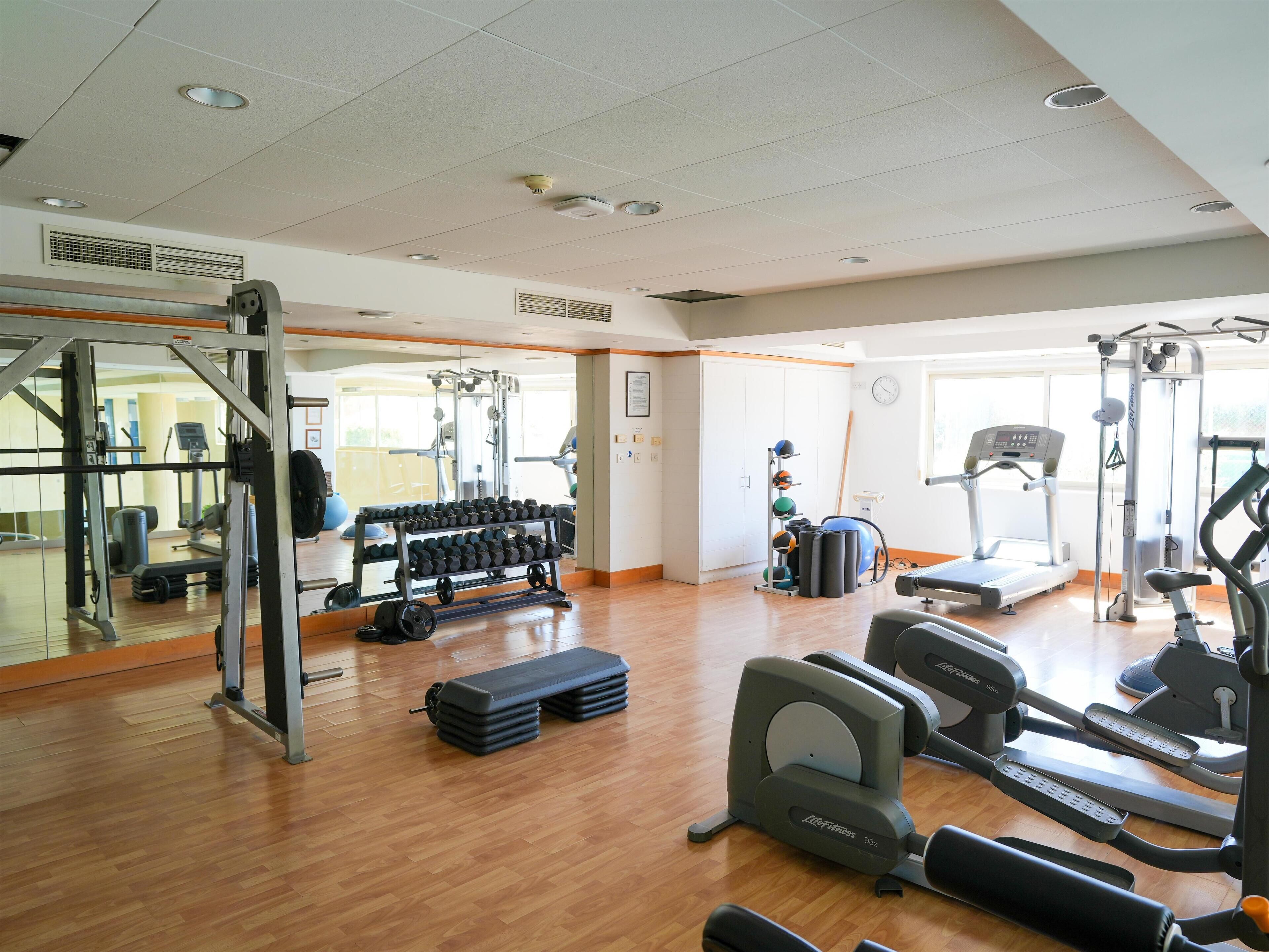 A gym with exercise equipment, a mirrored wall, and a wooden floor.