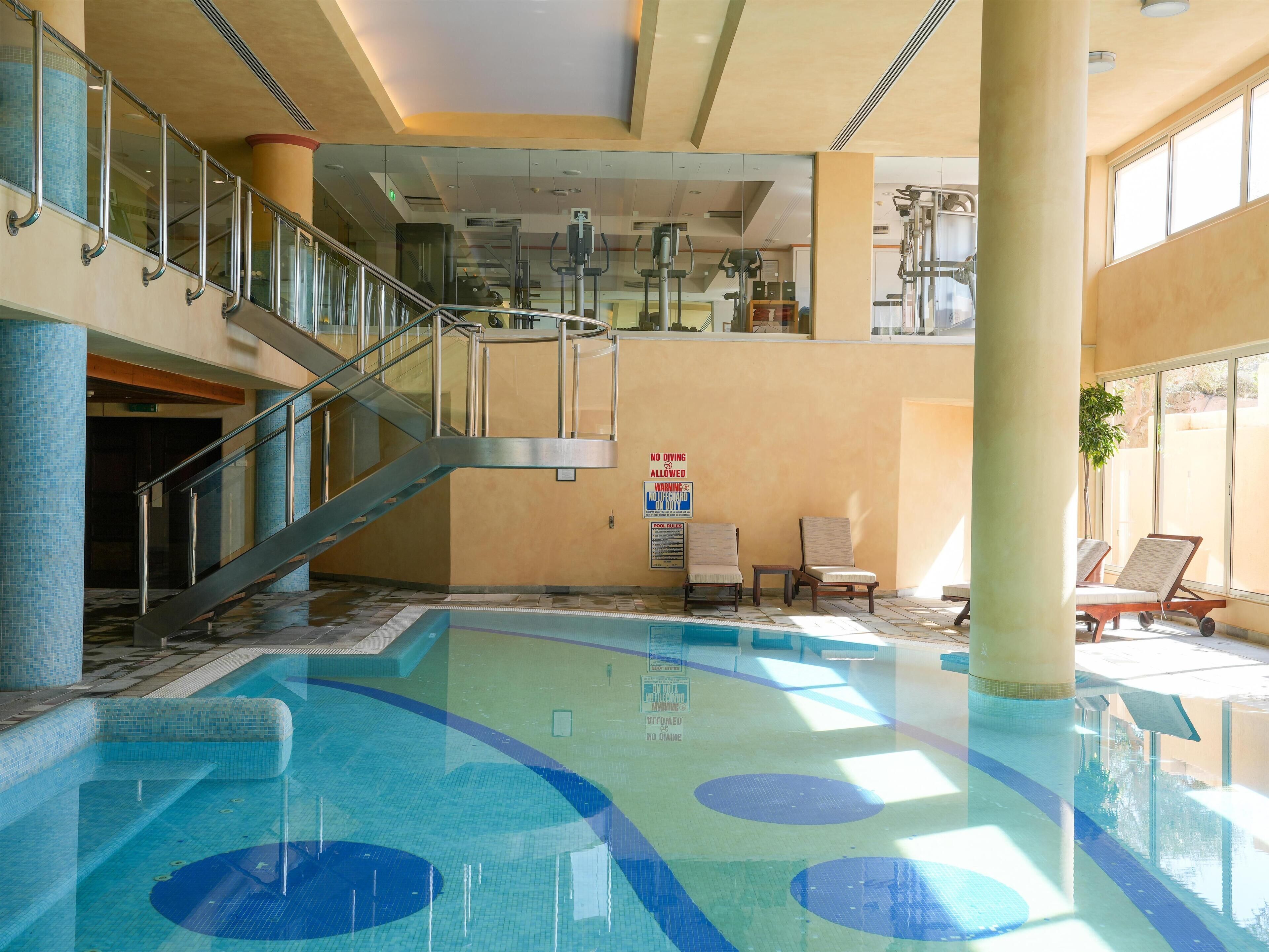 An indoor swimming pool with a glass barrier, a staircase, and lounge chairs.