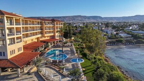 Um hotel com várias varandas, área de piscina com espreguiçadeiras e vista para o mar e a paisagem urbana.