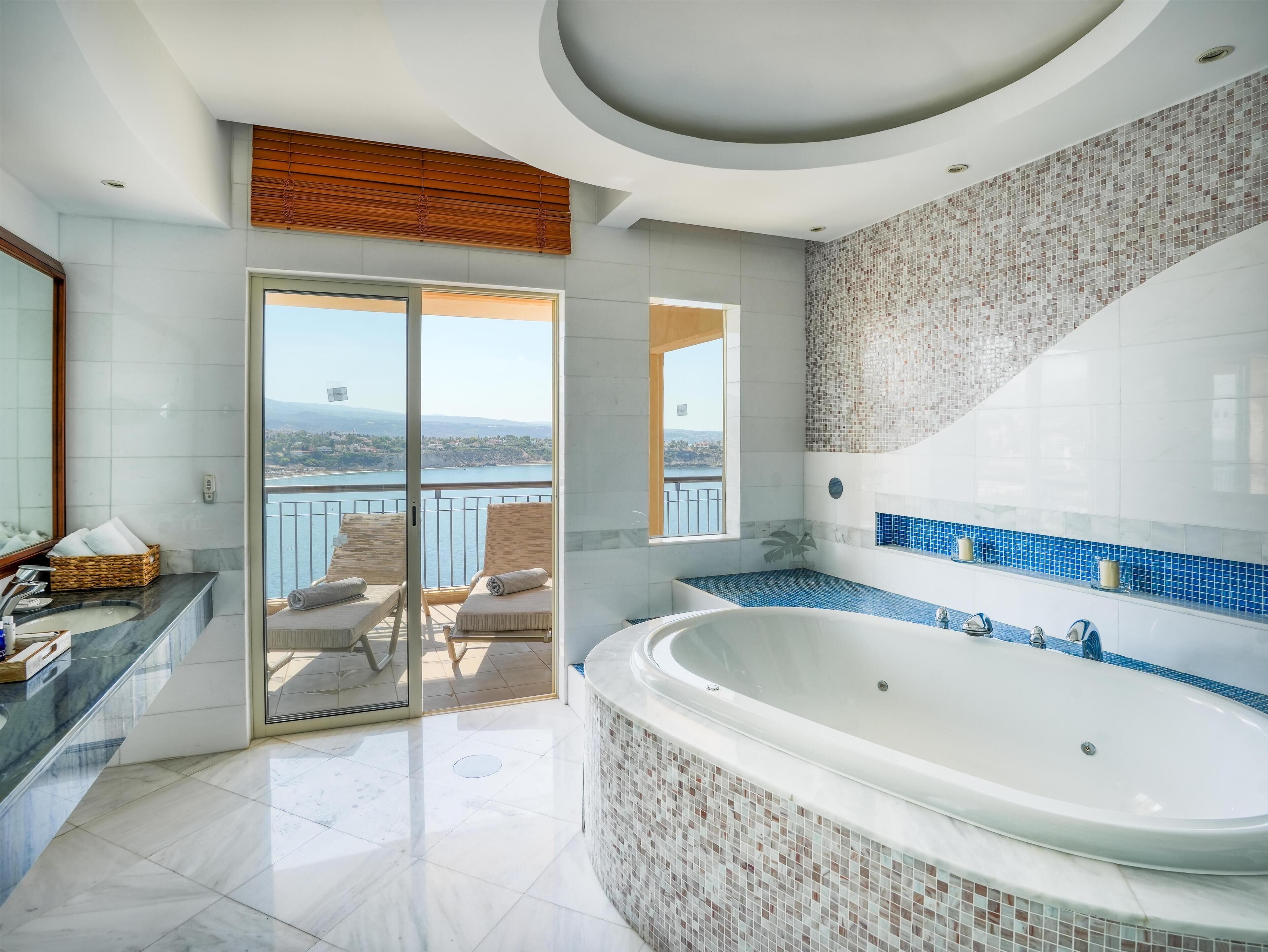 Un baño moderno con una bañera grande, un balcón con asientos y vistas a un lago.