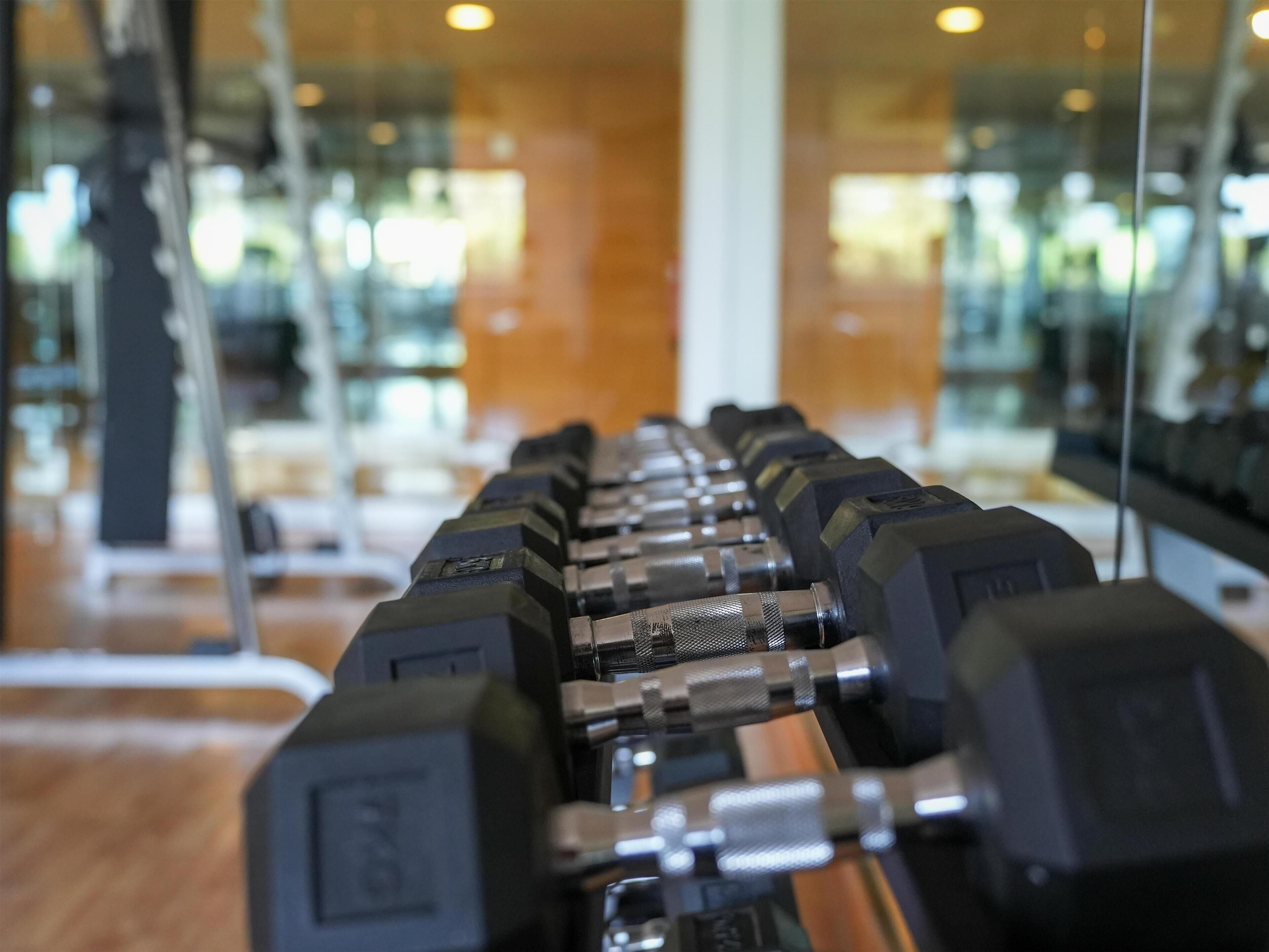 A row of dumbbells in a gym with mirrored walls and wooden flooring.